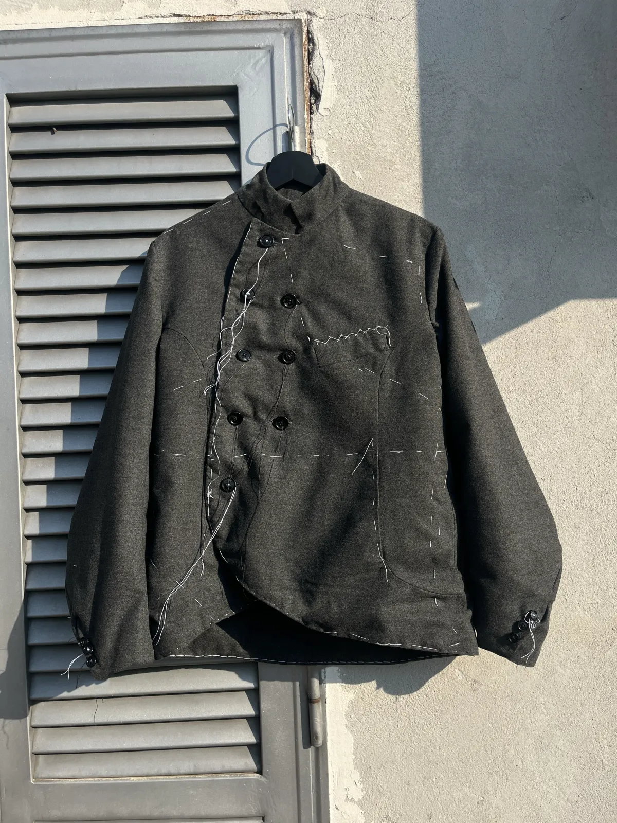 Handstitched Fencing Antique Jacket di Tommaso Curatella, fronte: giacca grigio scuro con collo alto e chiusura da scherma a 8 bottoni, con imbastiture a mano a vista